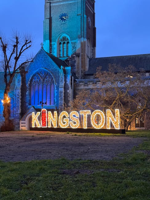 Nighttime view of Kingston, with illuminated signage spelling 'KINGSTON' in large, colorful letters placed on a grassy area in front of a historic church with tall stained-glass windows and a clock tower, under a dark sky. The scene highlights a clean and well-maintained public space, with surrounding trees and soft lighting emphasizing the area’s charm. This image relates to surface cleaning and maintenance in Kingston, reflecting a well-kept appearance associated with professional cleaning services offered by companies like carpetcleaningkingstonuponthames.org.uk.