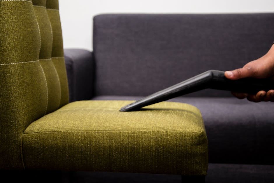 A woman with dark hair wearing a black uniform is holding two beige pillows, appearing to prepare for household cleaning or post-cleaning arrangement in a modern living room. The room features a light